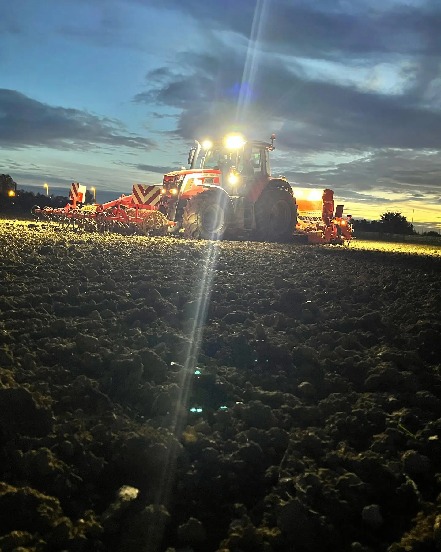 Tracteur travaillant le sol de nuit, phares allumés